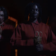 two evil teathered people in red jump suits holding scissors